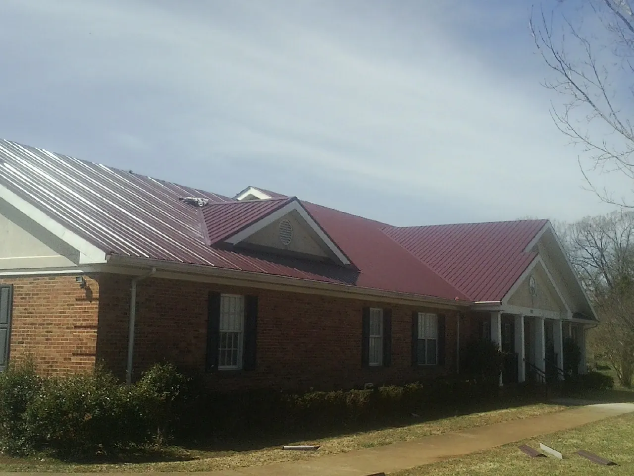 Red metal roof with gabled entries on a long brick building, from a Hail Damage Roof Repair job in Mcconnelsville