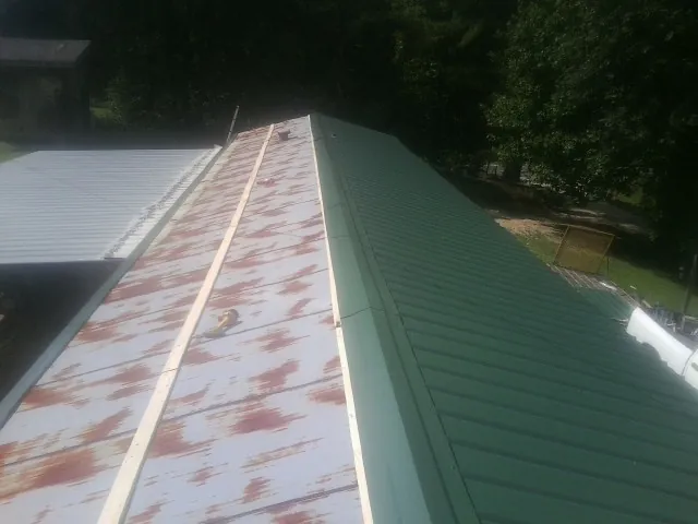 Old rusted panels beside newly installed green metal roofing — Wind Damage Roof Repair by Roofing Brothers in Mcconnelsville