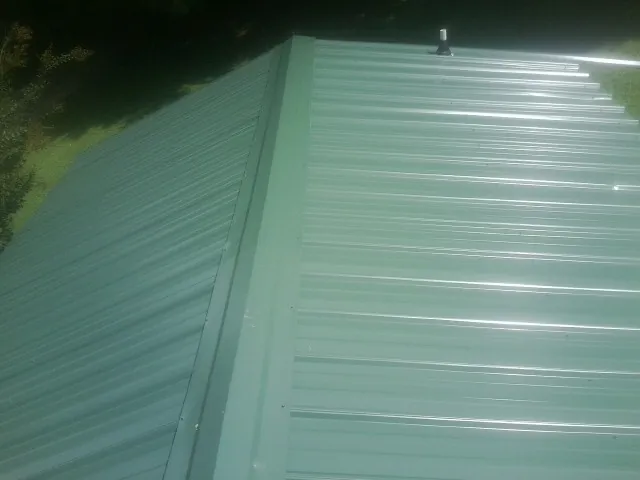 New green metal panels meeting at the ridge of a roof — Flat Roof Repair work by our crew in Mcconnelsville