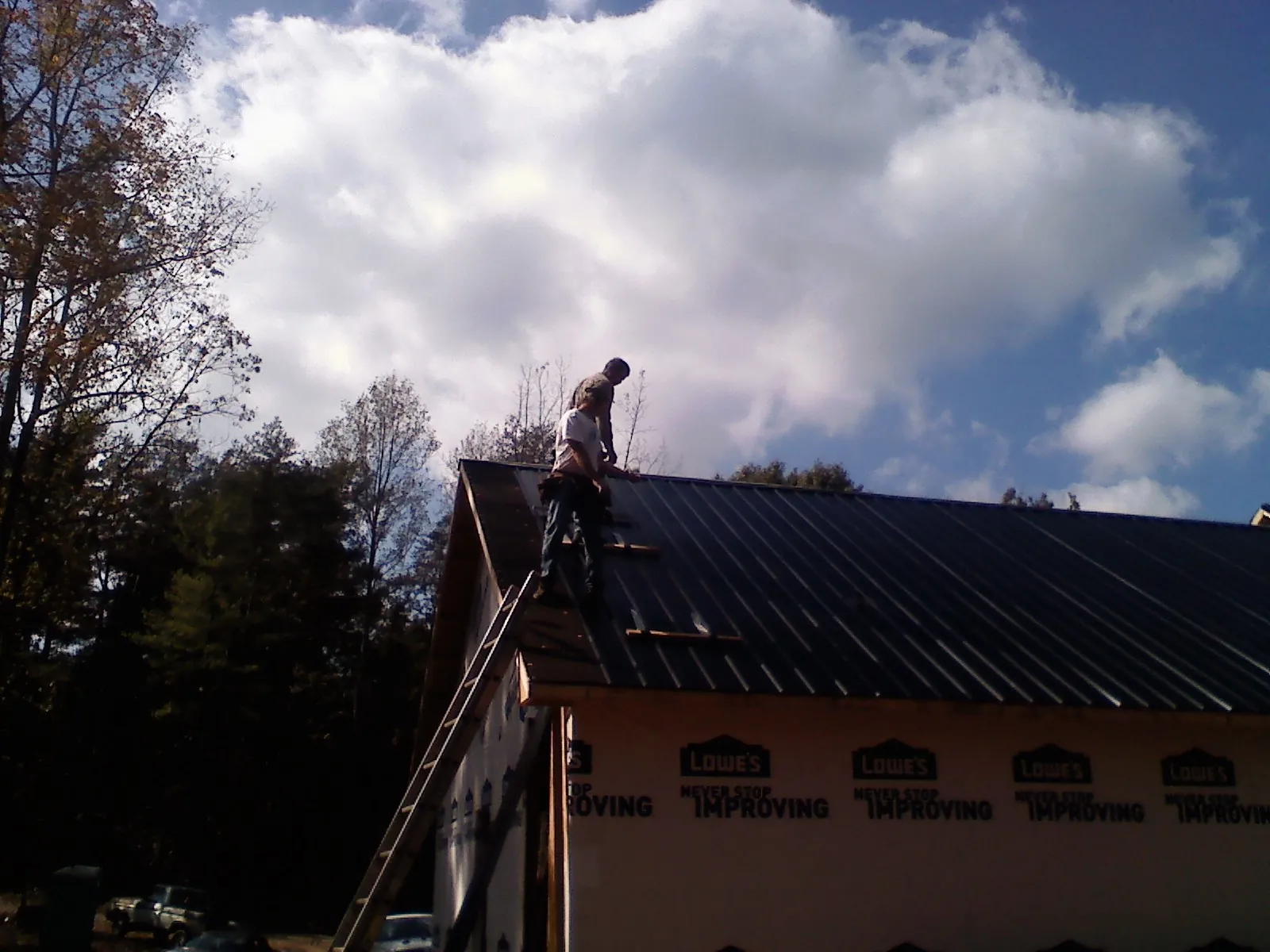 Roofer fastening dark metal panels high against a cloudy sky, from a Roof Inspection job in Mcconnelsville