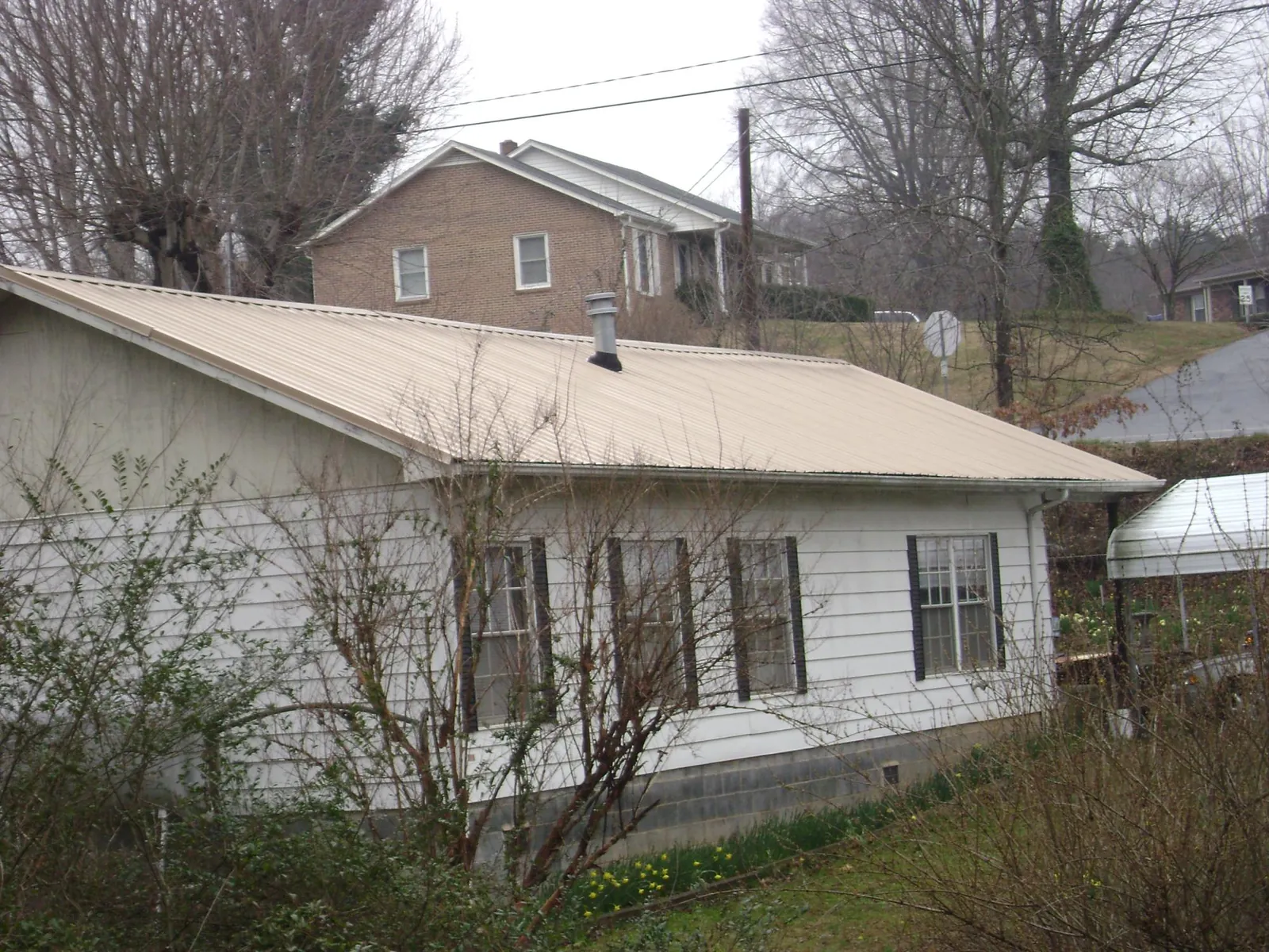 Tan metal roof on a white sided house set into a hillside — Commercial Roofing by Roofing Brothers in Mcconnelsville