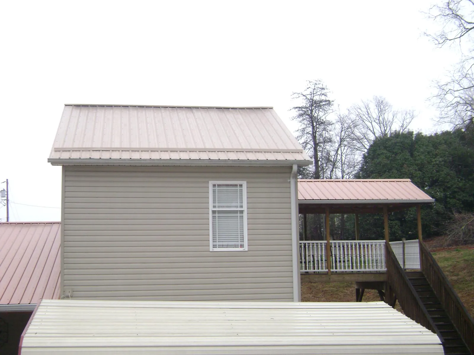 Tan metal roofs on a two story addition and attached porch, from a Roof Replacement job in Mcconnelsville